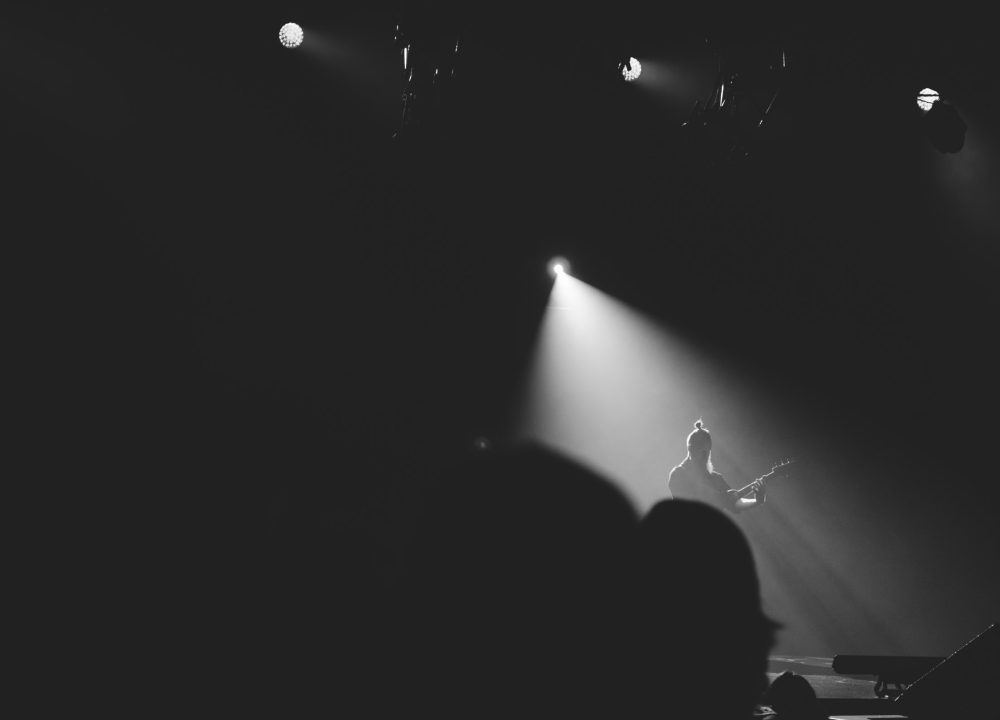 A lone figure under a single beam of light on a dark stage