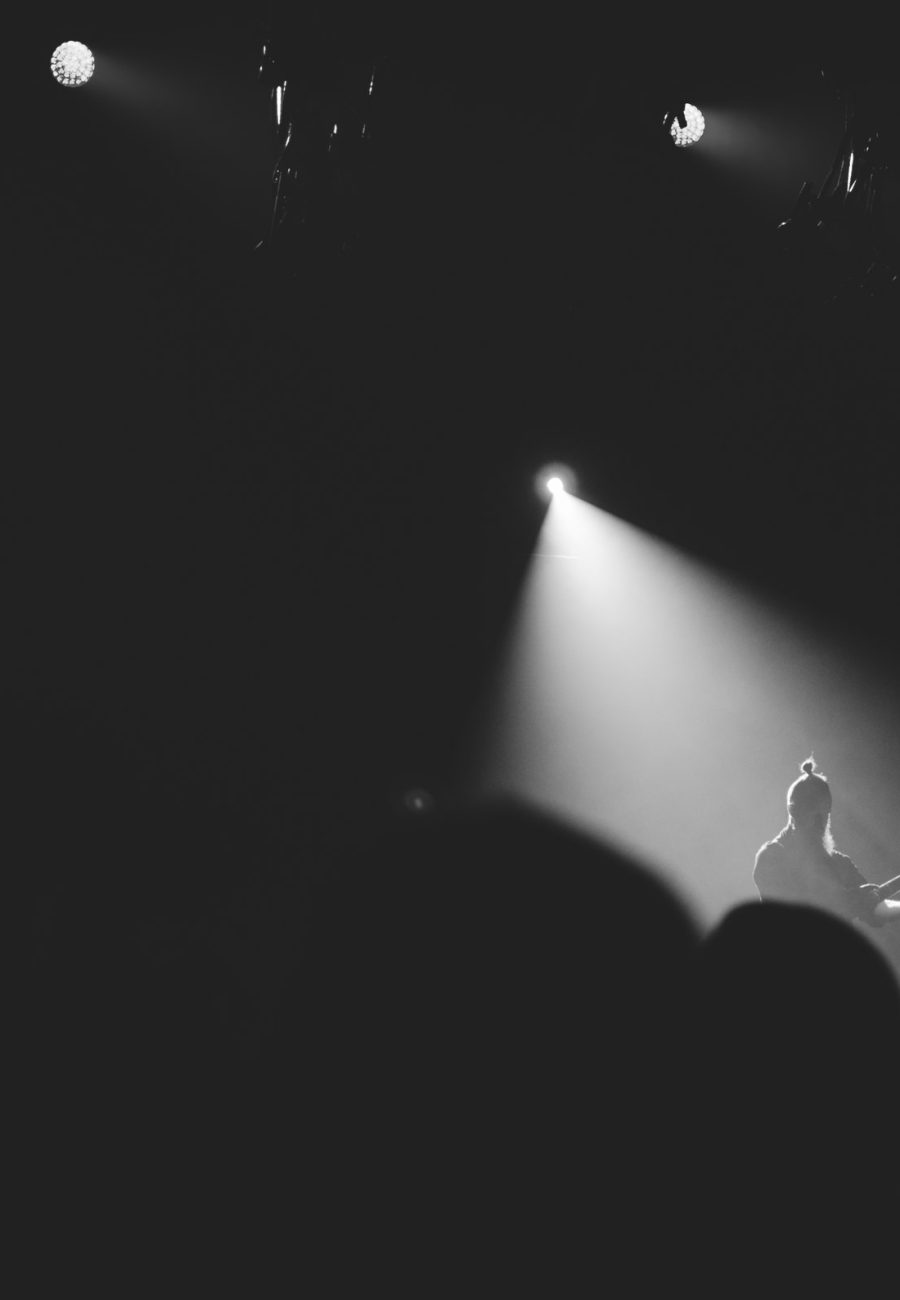A lone figure under a single beam of light on a dark stage