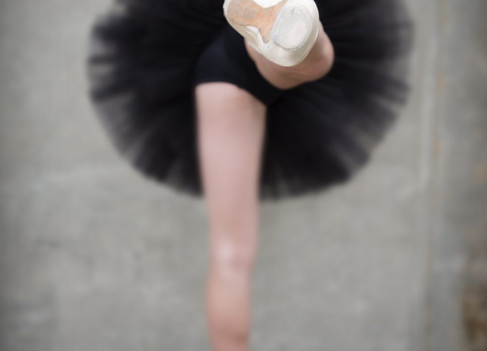 A dancer seen from behind against a concrete wall