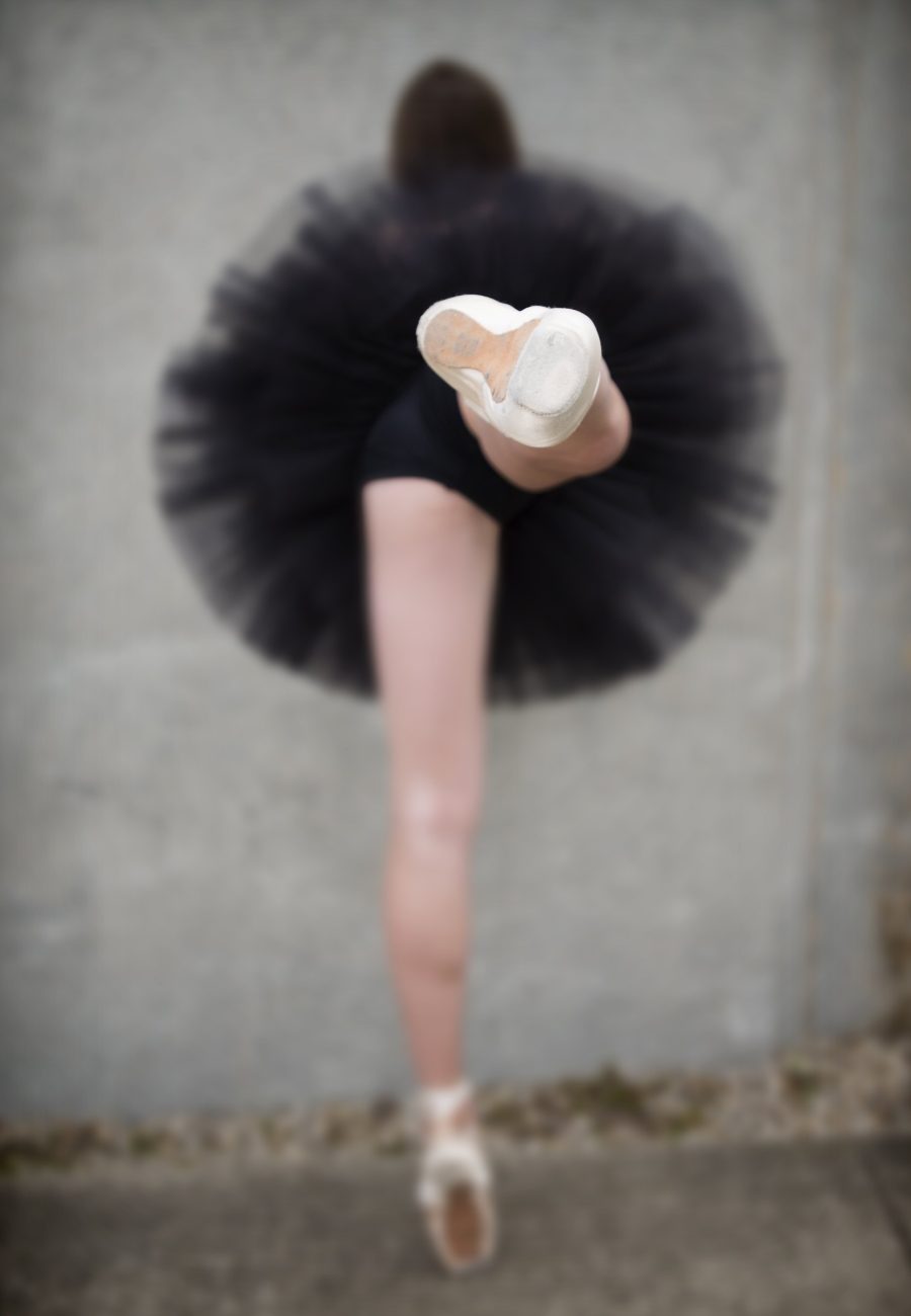A dancer seen from behind against a concrete wall